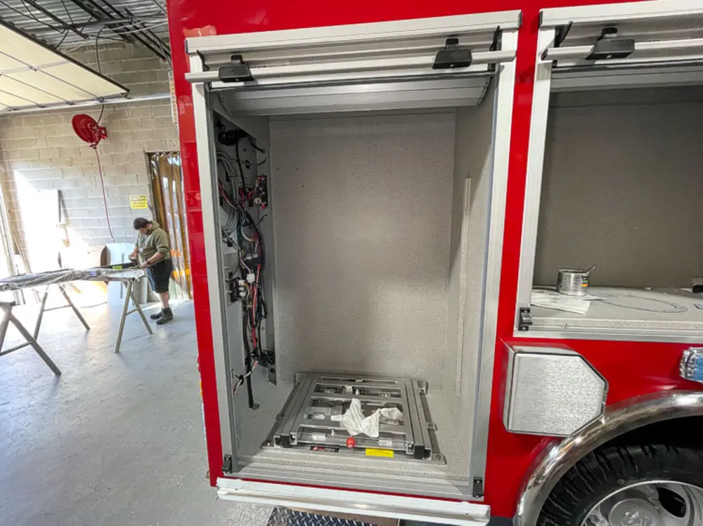 Exterior view of small fire truck showing cab, body compartments, and wheel/tire area.